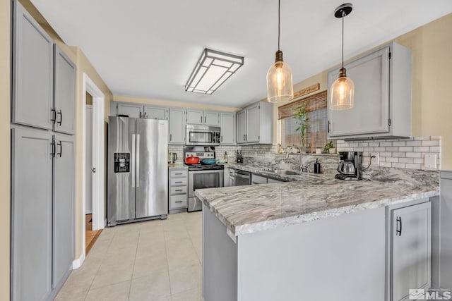 kitchen featuring decorative backsplash, hanging light fixtures, kitchen peninsula, stainless steel appliances, and light stone counters