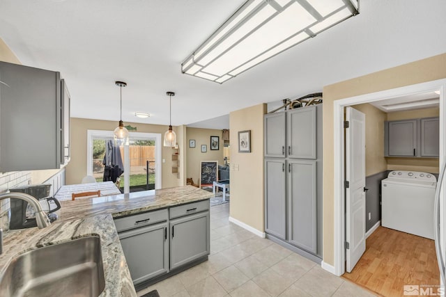 kitchen with washer / dryer, light stone countertops, sink, decorative light fixtures, and gray cabinets