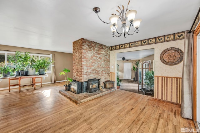 living room with ceiling fan with notable chandelier, hardwood / wood-style flooring, and a wood stove