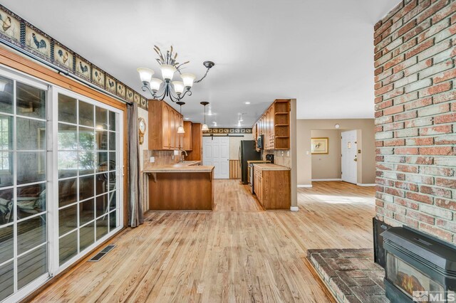 kitchen with kitchen peninsula, tasteful backsplash, decorative light fixtures, and light wood-type flooring