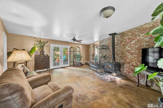 living room with french doors, a wood stove, concrete flooring, ceiling fan, and brick wall