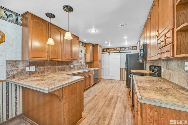 kitchen with black appliances, a barn door, kitchen peninsula, decorative light fixtures, and light hardwood / wood-style flooring