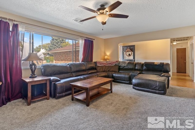 carpeted living room featuring ceiling fan and a textured ceiling