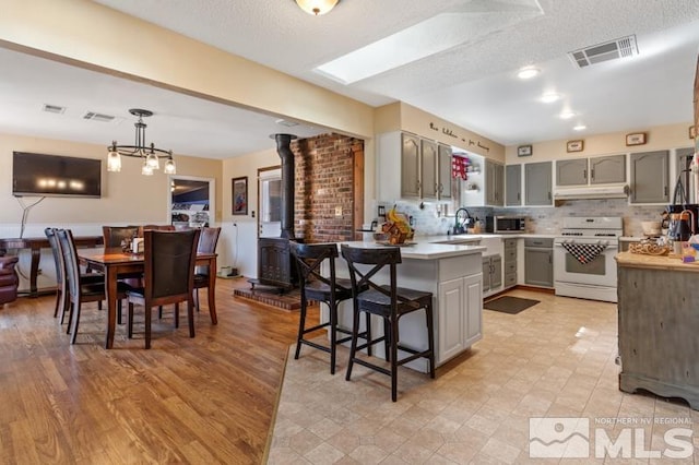 kitchen featuring gray cabinets, a wood stove, decorative light fixtures, and white range oven