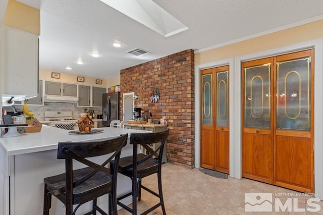 kitchen with kitchen peninsula, stainless steel fridge, backsplash, white gas stove, and a kitchen bar