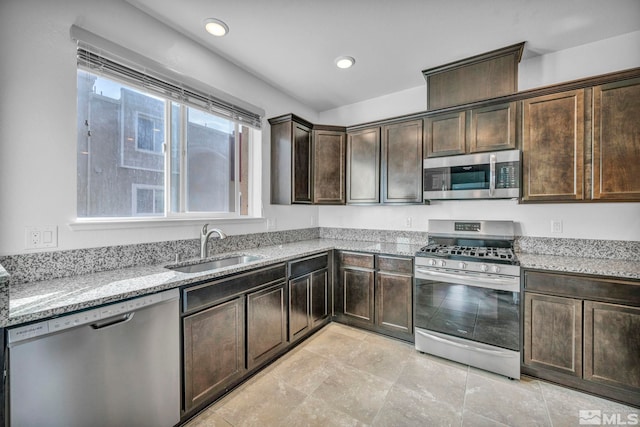 kitchen with dark brown cabinets, light stone countertops, stainless steel appliances, and sink