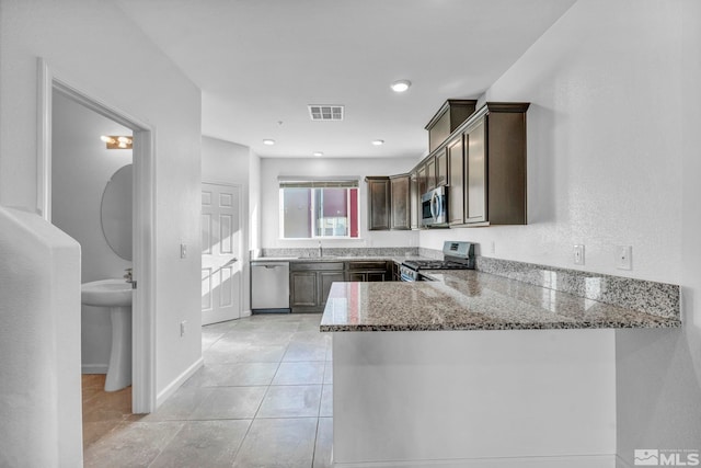 kitchen with stone countertops, kitchen peninsula, dark brown cabinets, sink, and appliances with stainless steel finishes