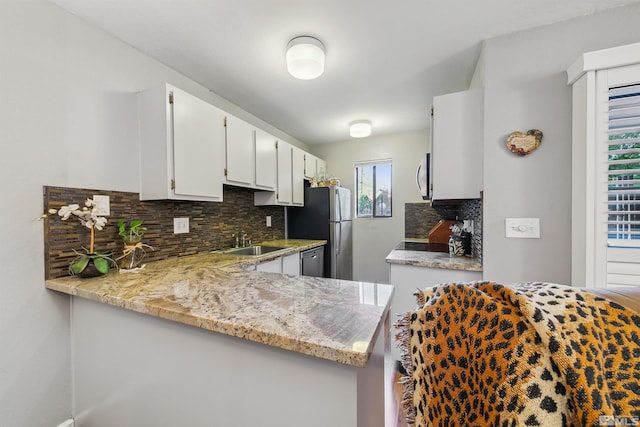 kitchen with kitchen peninsula, decorative backsplash, white cabinets, appliances with stainless steel finishes, and sink