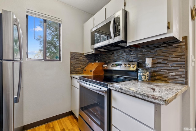 kitchen featuring decorative backsplash, white cabinets, stainless steel appliances, and light wood-type flooring