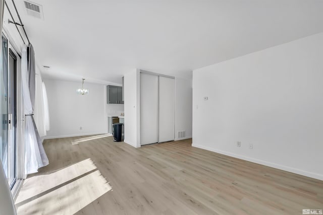 unfurnished living room with a chandelier and light wood-type flooring