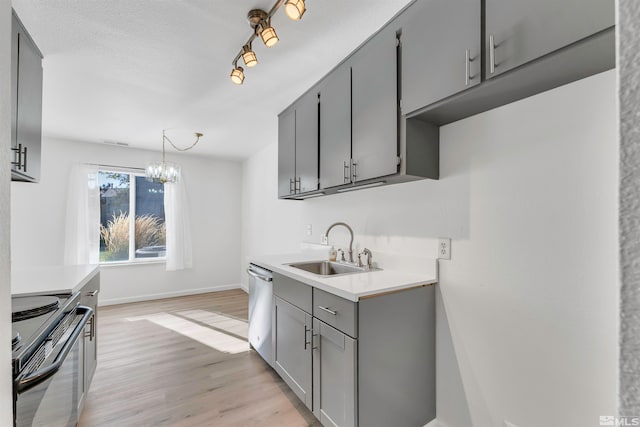 kitchen with appliances with stainless steel finishes, sink, gray cabinets, decorative light fixtures, and light hardwood / wood-style floors