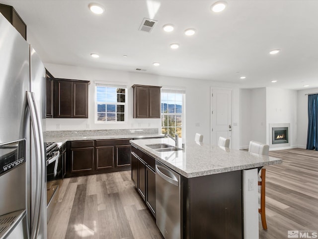 kitchen with sink, a kitchen breakfast bar, stainless steel appliances, light hardwood / wood-style flooring, and a kitchen island with sink