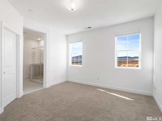 unfurnished bedroom with a closet, a mountain view, light colored carpet, and connected bathroom