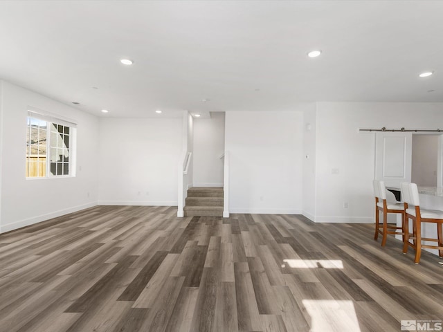 unfurnished living room with a barn door and dark hardwood / wood-style flooring