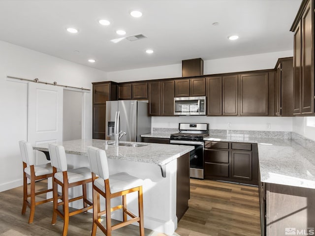 kitchen with dark hardwood / wood-style floors, a center island with sink, sink, a barn door, and appliances with stainless steel finishes