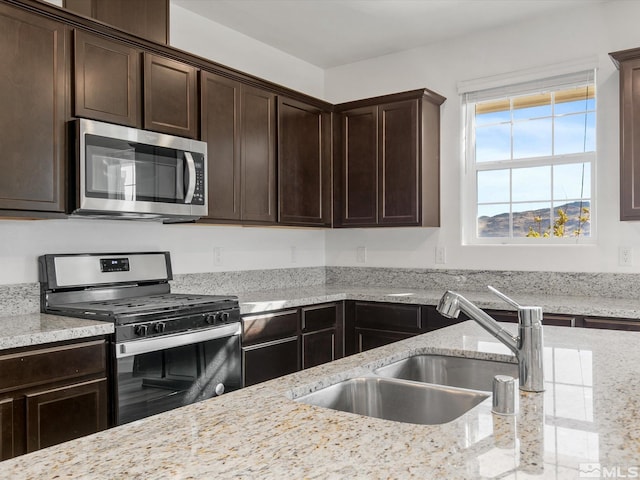 kitchen with dark brown cabinets, stainless steel appliances, sink, and light stone counters