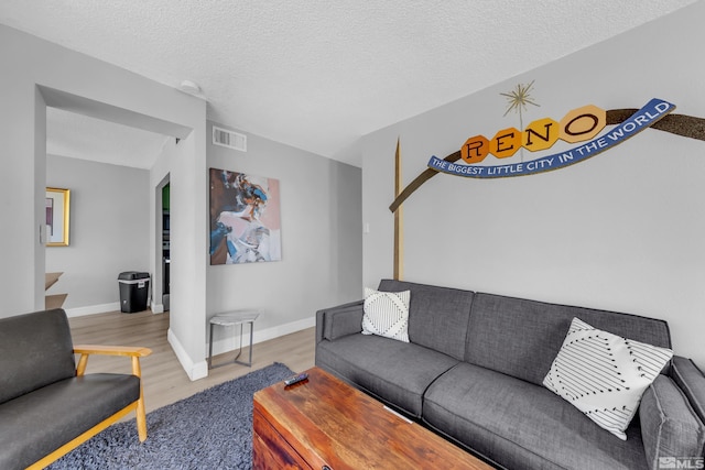 living room featuring a textured ceiling, visible vents, wood finished floors, and baseboards