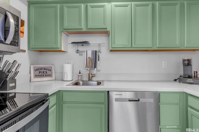 kitchen featuring green cabinetry, stainless steel appliances, light countertops, and a sink