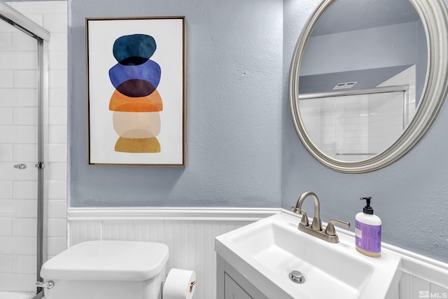 bathroom featuring toilet, a tile shower, a textured wall, and wainscoting
