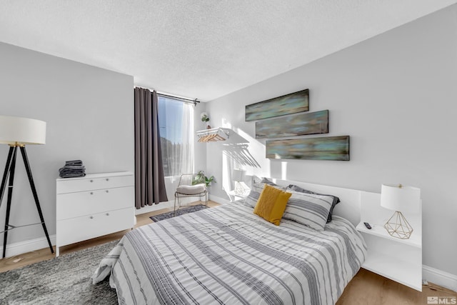 bedroom with a textured ceiling, wood finished floors, and baseboards