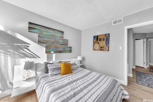 bedroom featuring wood finished floors, visible vents, baseboards, and a textured ceiling