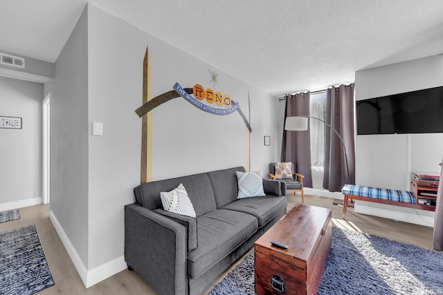 living area featuring wood finished floors, visible vents, baseboards, and a textured ceiling