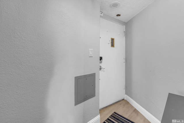 doorway to outside with baseboards, a textured ceiling, and light wood finished floors