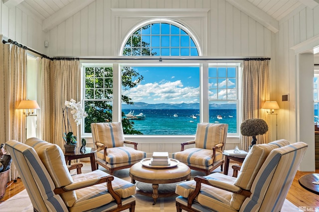 sitting room featuring beam ceiling, light hardwood / wood-style flooring, a water view, high vaulted ceiling, and wood walls