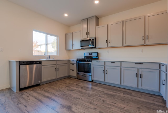 kitchen with appliances with stainless steel finishes, hardwood / wood-style floors, sink, and gray cabinets