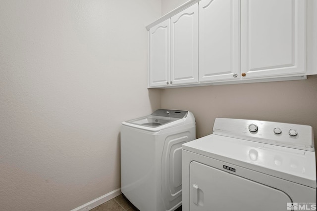 washroom with dark tile patterned flooring, washer and dryer, and cabinets