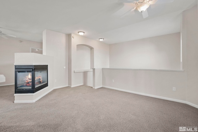 unfurnished living room featuring ceiling fan, carpet floors, and a multi sided fireplace