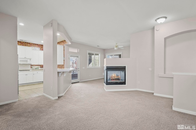 unfurnished living room with a multi sided fireplace, light colored carpet, and ceiling fan