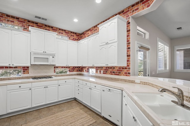 kitchen featuring white appliances, sink, kitchen peninsula, white cabinets, and brick wall