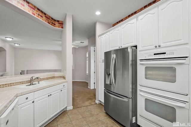 kitchen featuring tile countertops, sink, light tile patterned floors, white cabinetry, and white appliances