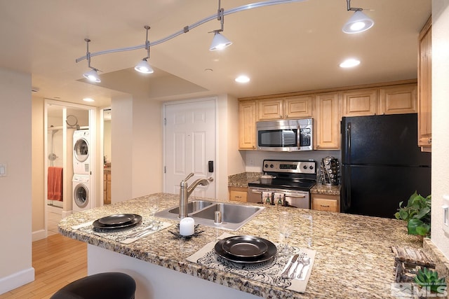 kitchen featuring appliances with stainless steel finishes, sink, light stone countertops, light hardwood / wood-style floors, and stacked washer and dryer