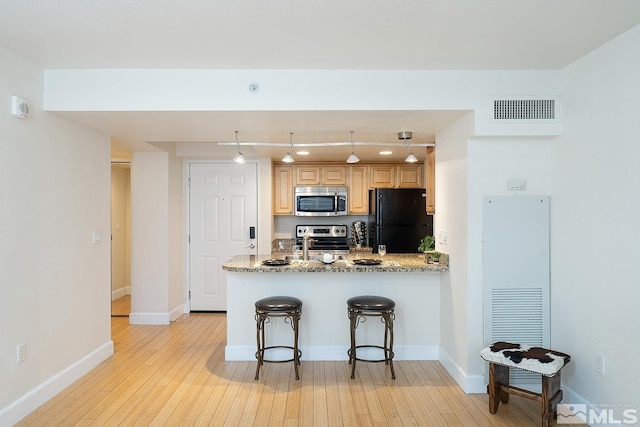 kitchen with kitchen peninsula, rail lighting, stainless steel appliances, light stone counters, and light hardwood / wood-style flooring