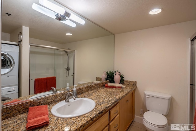 bathroom featuring stacked washer and clothes dryer, toilet, tile patterned flooring, a shower with shower door, and vanity