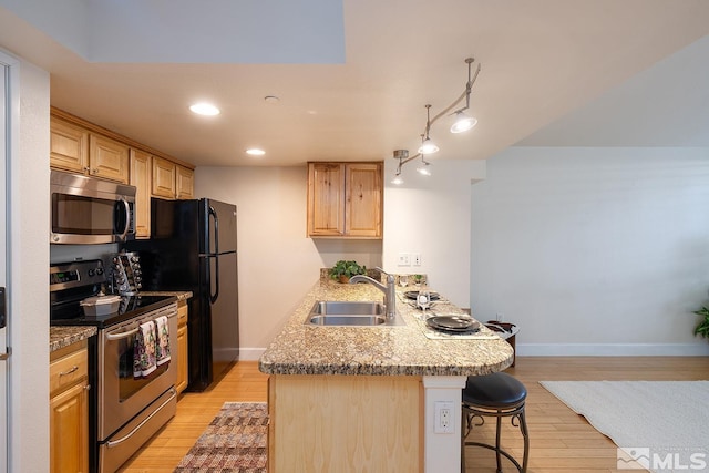 kitchen featuring a breakfast bar area, light hardwood / wood-style flooring, kitchen peninsula, stainless steel appliances, and sink