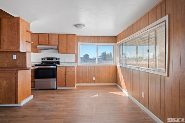 kitchen featuring wooden walls, stainless steel electric range oven, and light wood-type flooring