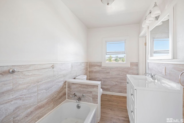 bathroom with a tub, hardwood / wood-style floors, toilet, tile walls, and vanity