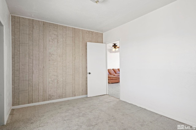 unfurnished room featuring light carpet, wooden walls, and ceiling fan