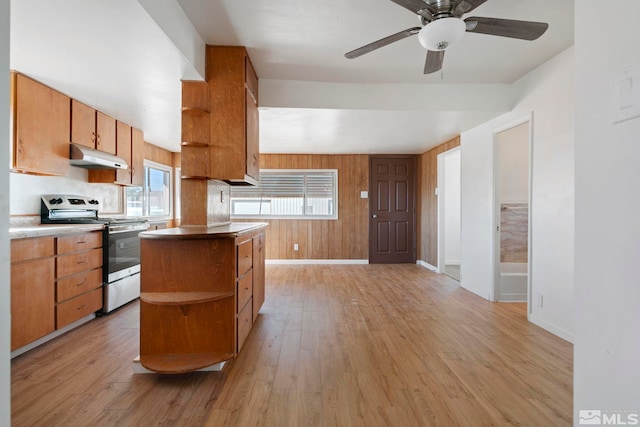 kitchen with ceiling fan, wooden walls, stainless steel range with electric stovetop, a center island, and light hardwood / wood-style floors