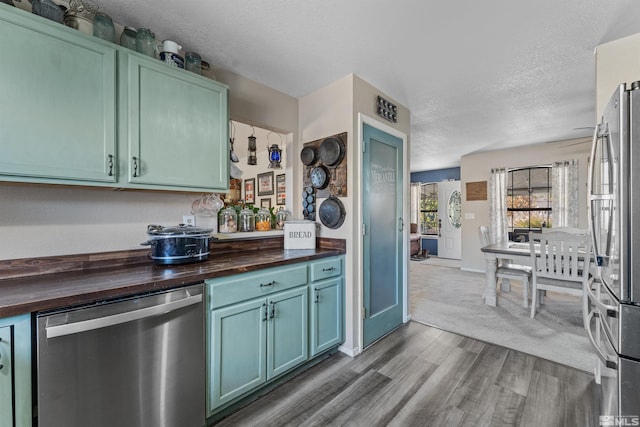 kitchen with appliances with stainless steel finishes, wood counters, hardwood / wood-style flooring, and a textured ceiling