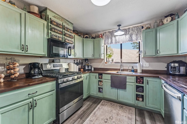kitchen with dark wood-type flooring, appliances with stainless steel finishes, green cabinets, and wooden counters