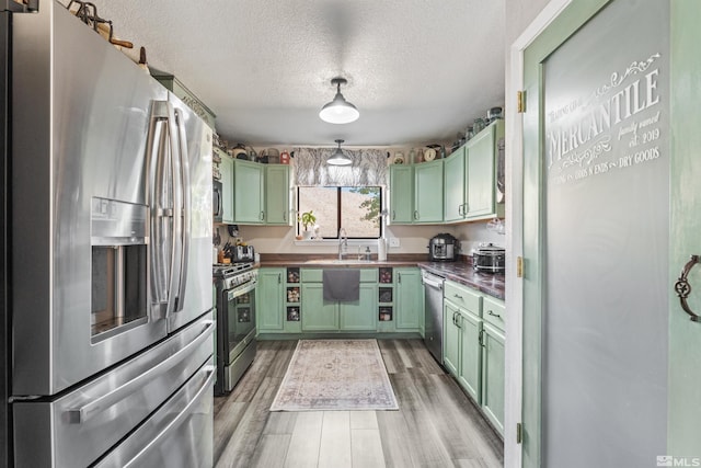 kitchen with green cabinets, a textured ceiling, stainless steel appliances, and light hardwood / wood-style floors