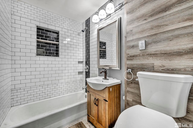 full bathroom with vanity, tiled shower / bath combo, toilet, and wood walls