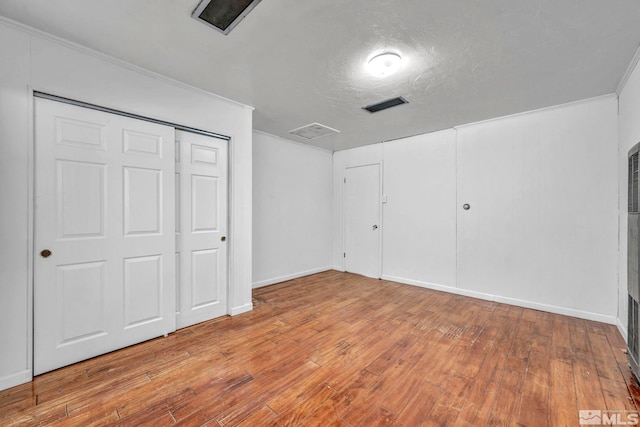 unfurnished bedroom featuring ornamental molding, light hardwood / wood-style flooring, a textured ceiling, and a closet