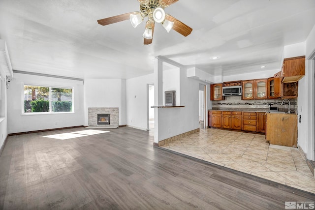 kitchen featuring a stone fireplace, backsplash, sink, light wood-type flooring, and ceiling fan