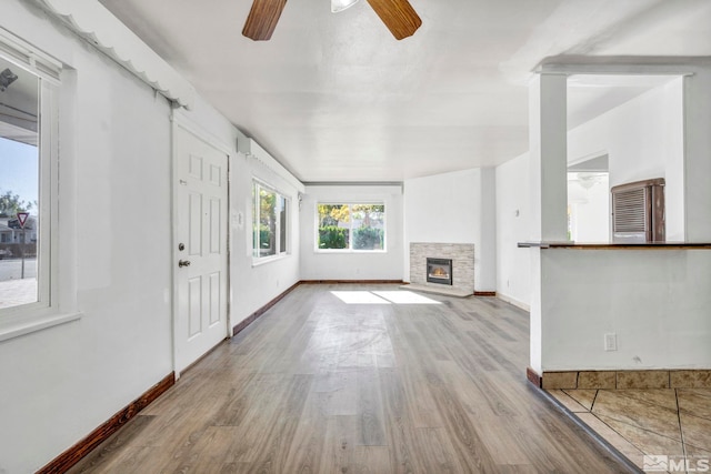 unfurnished living room featuring light hardwood / wood-style floors, a stone fireplace, and ceiling fan