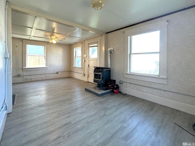 unfurnished living room featuring wood-type flooring, a wood stove, and ceiling fan